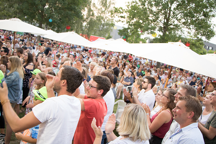 Donaufest 2019 in Deggendorf – Publikum unter Sonnenschirmen Dichtes Publikum unter großen Sonnenschirmen bei einer sommerlichen Veranstaltung im Freien; mehrere Menschen applaudieren und blicken zur Bühne.