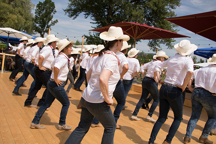 Donaufest 2019: Line-Dance-Auftritt im Freien Tanzgruppe mit weißen Cowboyhüten und weißen Hemden bei einem Line-Dance-Auftritt auf einer sommerlichen Festfläche