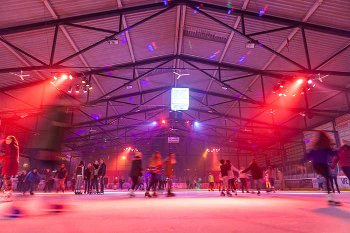 Menschen laufen bei der Eiszeit 2019 in Deggendorf unter farbiger Beleuchtung Schlittschuh auf einer Eislauffläche in einer Halle.