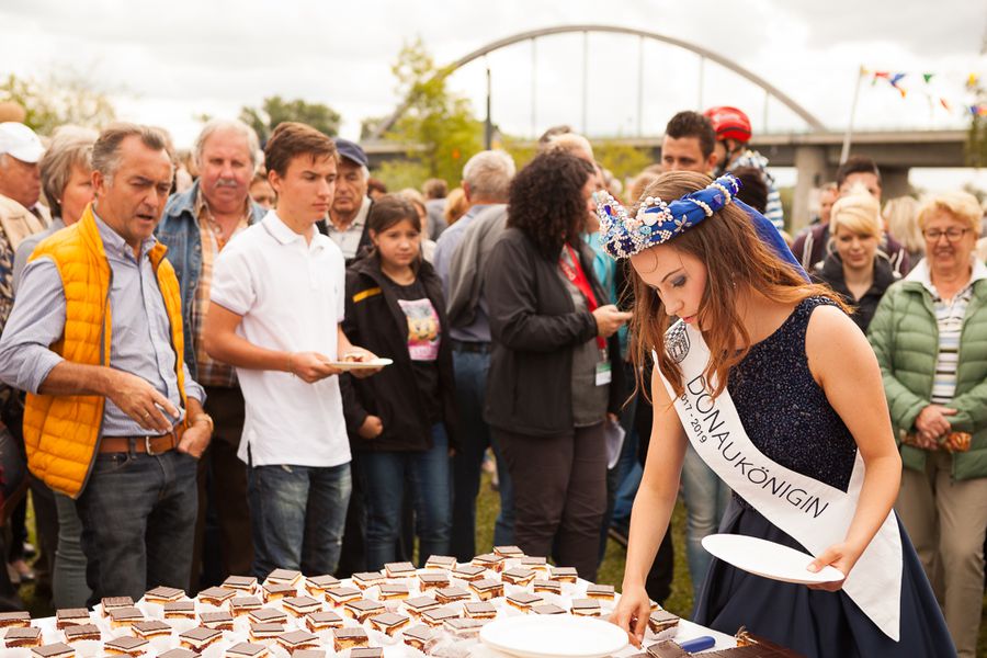 Königin beim Verteilen von Kuchen auf einem Vereinsfest Eine gekrönte junge Frau mit Schärpe verteilt Kuchenstücke an einem Tisch, während Menschen zuschauen.