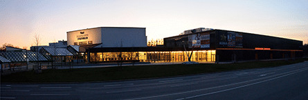 Breite Außenansicht einer modernen Stadthalle mit beleuchteten Glasfronten bei Abendlicht