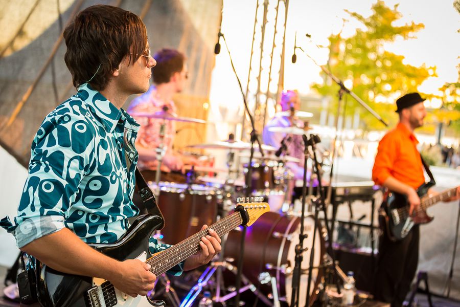 Live-Konzert des Vereins DE G – Saison 2025 Gitarrist und Bassist spielen bei einem Open-Air-Konzert auf einer Bühne; im Hintergrund sind Schlagzeug und weitere Musikinstrumente zu sehen.