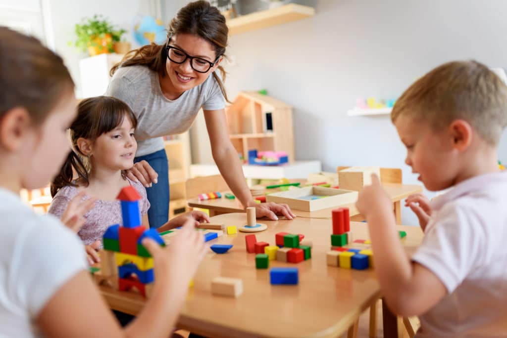 Kinder beim Spielen im Kindergarten Eine Erzieherin spielt und baut gemeinsam mit drei Kindern an einem Tisch mit bunten Holzbausteinen.