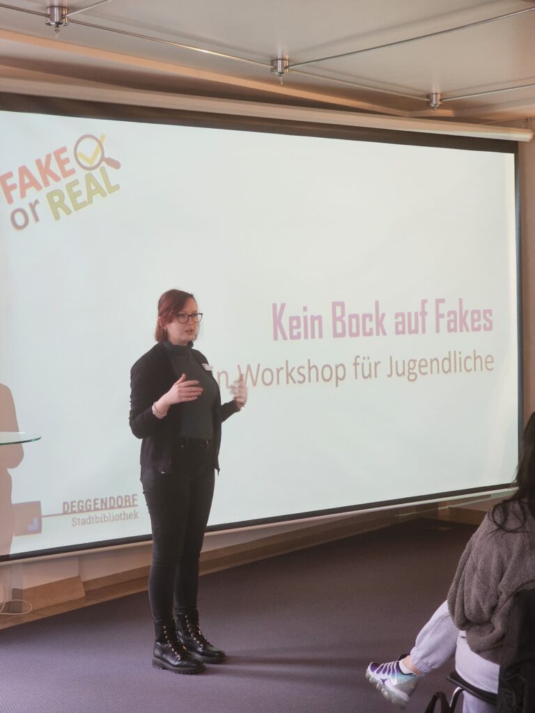 Eine Referentin spricht vor einer Leinwand mit dem Titel „Kein Bock auf Fakes – Workshop für Jugendliche“; links ist das Logo der Stadtbibliothek Deggendorf zu sehen.