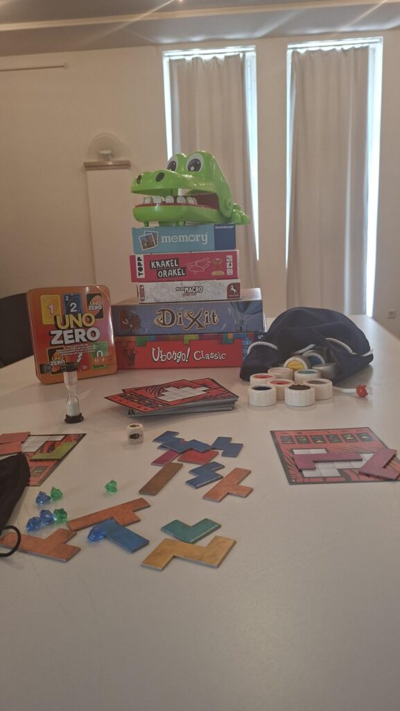 Tisch mit verschiedenen Brettspielen, bunten Puzzleteilen, Spielsteinen und einem grünen Krokodil-Spielzeug