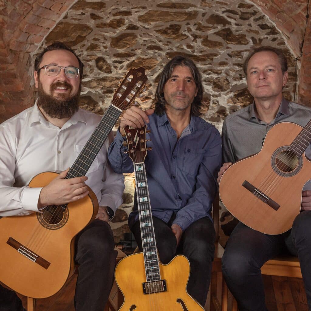 Drei Musiker des Chillout Trios Puente mit akustischen Gitarren vor einer steinernen Gewölbewand