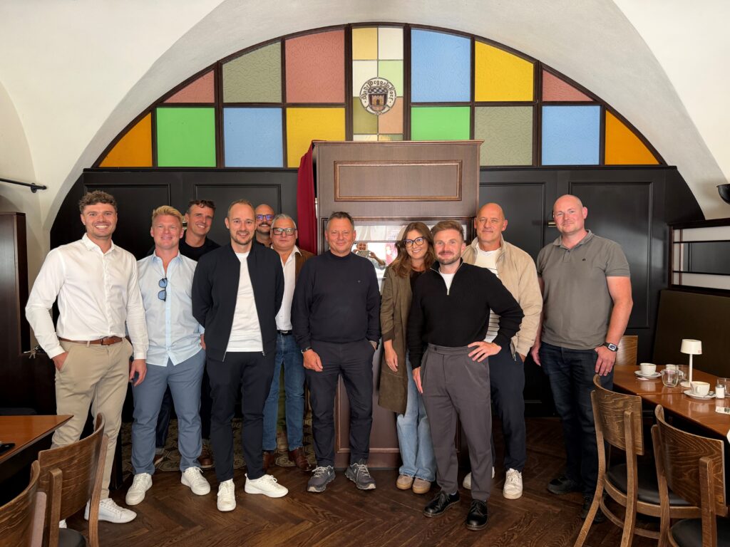 Gruppe von zehn Personen posiert in einem Café vor einem farbigen Buntglasfenster.