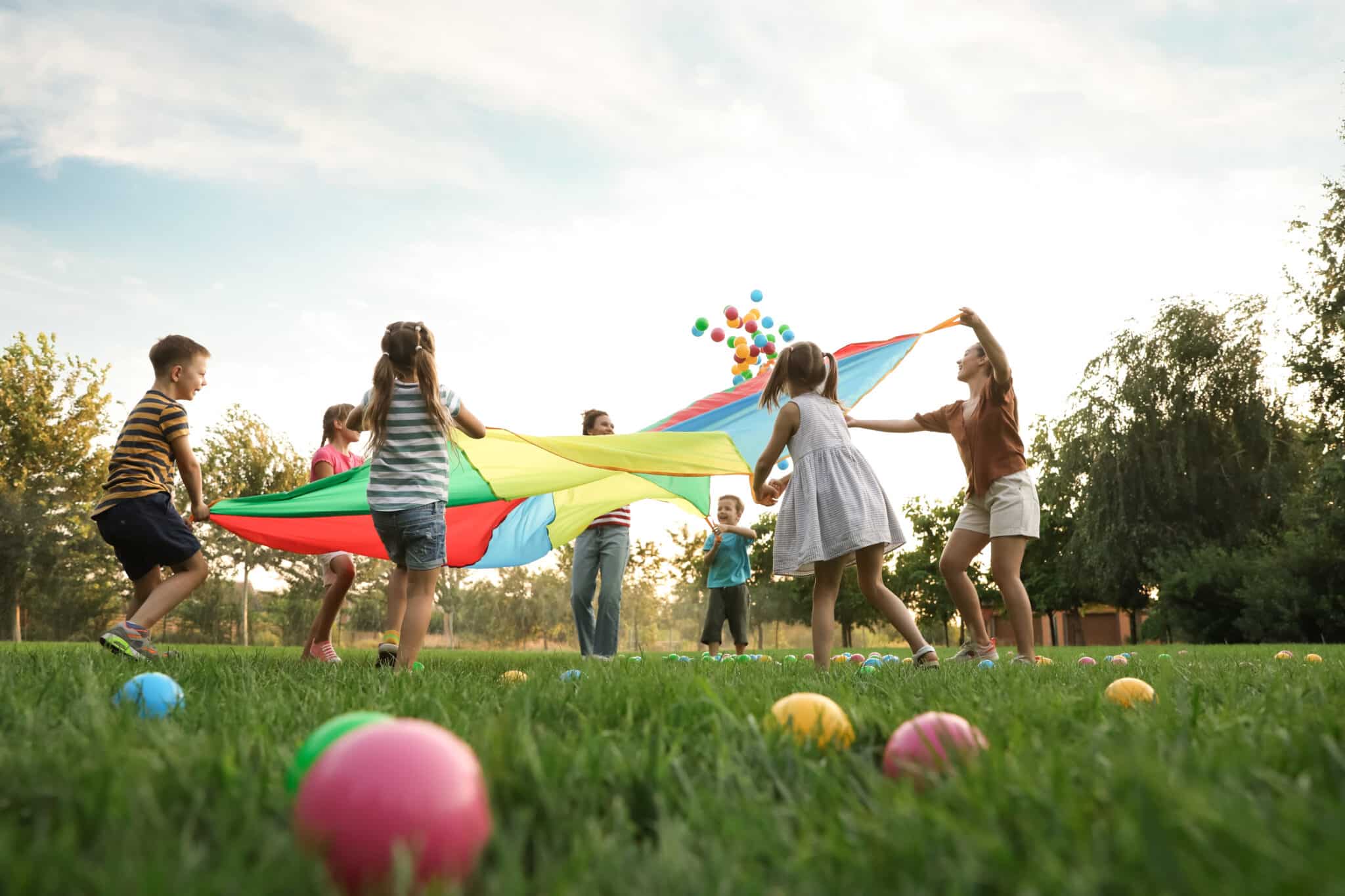 Kinder und Jugendliche beim Vereinssommerfest in Deggendorf Kinder und Jugendliche spielen auf einer Wiese mit einem bunten Schwungtuch; im Vordergrund liegen farbige Bälle.