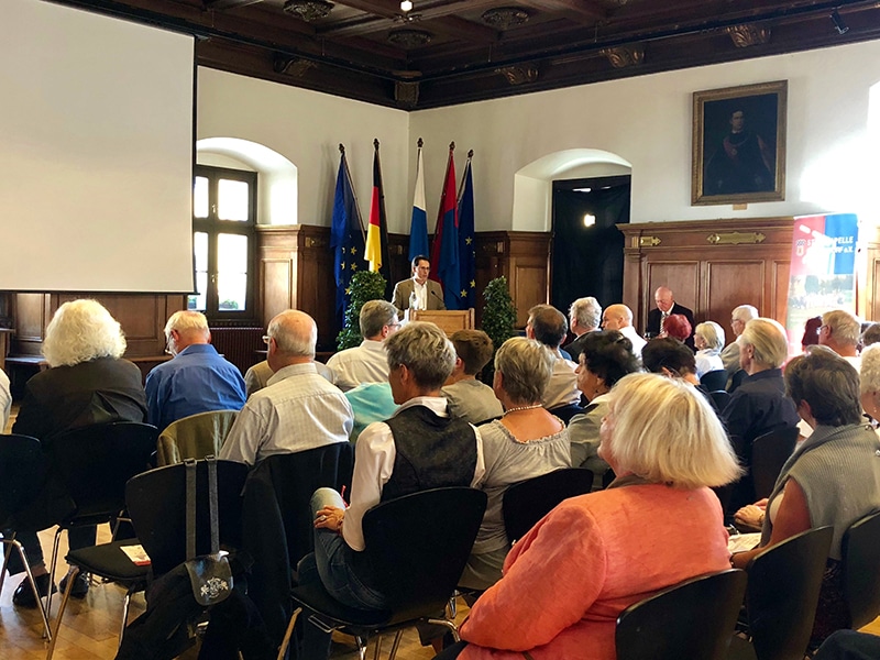 Publikum bei einer Veranstaltung zum Tag der Heimat im historischen Saal mit Rednerpult, Deutschland- und Europaflagge sowie weiteren Fahnen