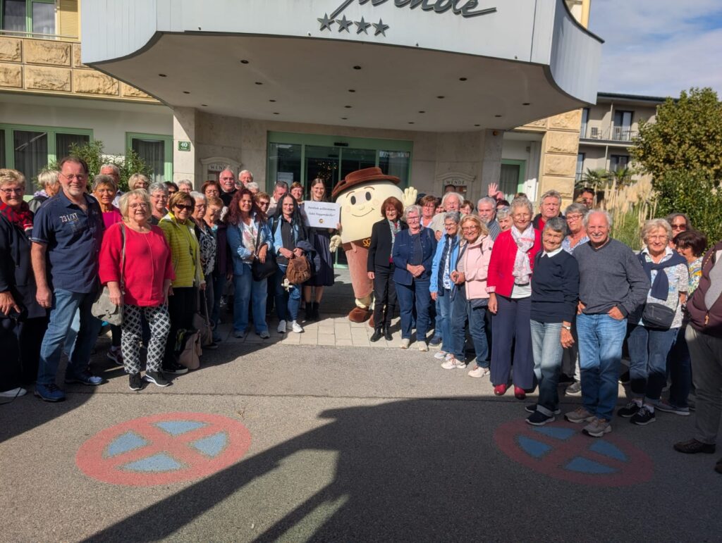 Reisegruppe mit Maskottchen vor dem Eingang eines Hotels