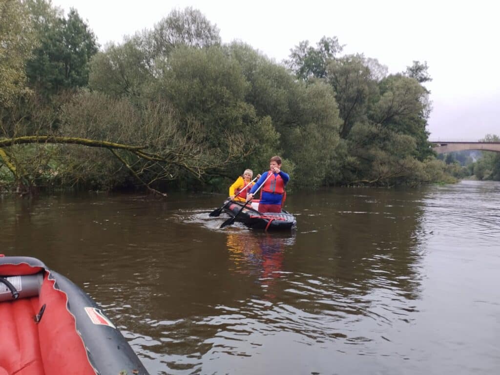 Zwei Personen in einem Schlauchkanu paddeln auf dem Fluss Regen; am linken Bildrand ist ein weiteres rotes Schlauchboot zu sehen.