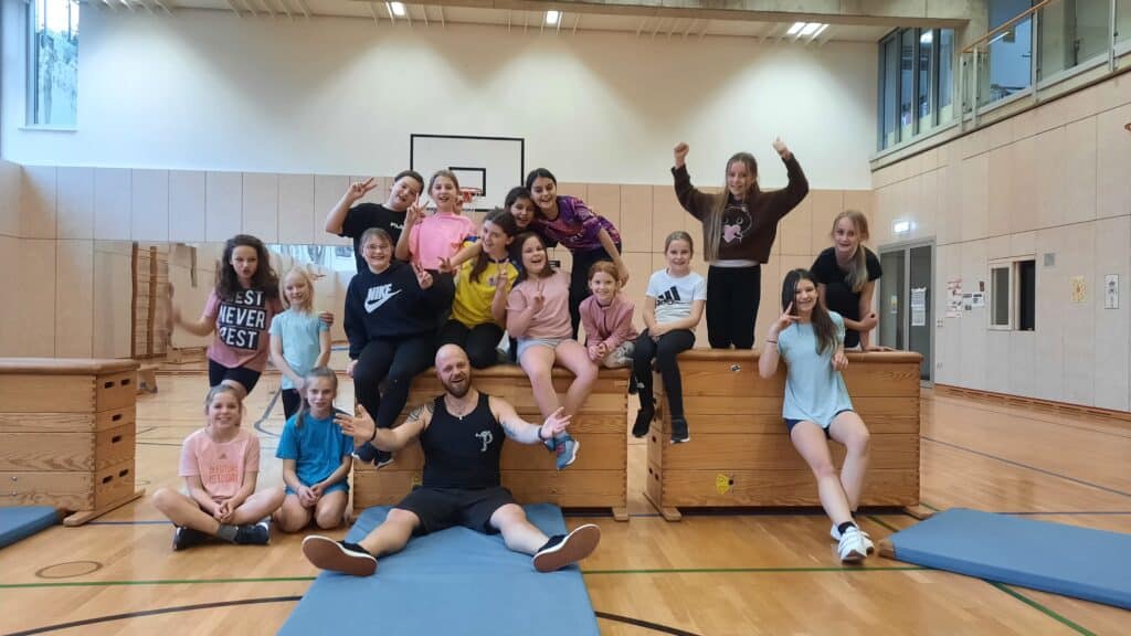 4You-Parkour an der Realschule Maria Ward Gruppe aus Jugendlichen und einem Erwachsenen posiert auf Turnkästen in einer Sporthalle.