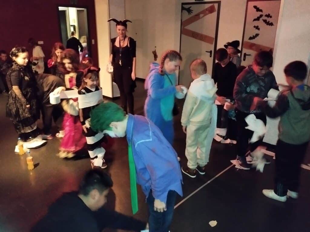 Verkleidete Kinder und Erwachsene nehmen in einem Innenraum an einer Halloween-Veranstaltung teil.