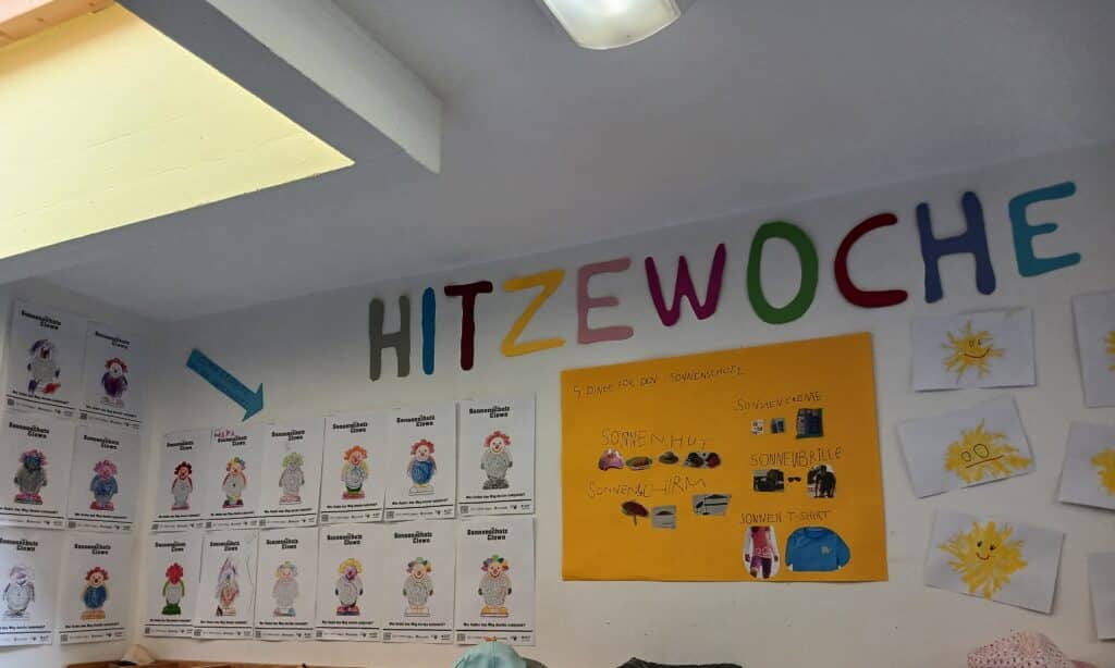 Wanddekoration zur Hitzewoche mit bunten Schriftzügen, Kinderzeichnungen und Informationsplakat