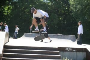 Skateboarder springt auf einer Skateanlage über eine Rampe, während weitere Jugendliche zuschauen.