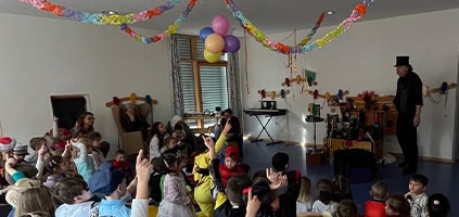 Zauberer Martini bei einer Kinderveranstaltung Ein Zauberer mit schwarzem Zylinder steht in einem dekorierten Raum vor einer Gruppe sitzender Kinder.