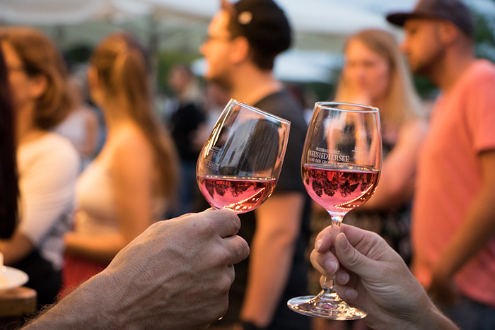 Donaufest 2019: Anstoßen mit Wein Zwei Personen stoßen bei einer Veranstaltung mit Weingläsern an; im Hintergrund stehen weitere Gäste.