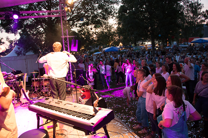 Donaufest 2019 in Deggendorf – Konzertpublikum vor der Bühne Musiker auf einer beleuchteten Bühne mit Keyboard und Schlagzeug, davor ein dichtes Publikum bei einem Open-Air-Konzert.
