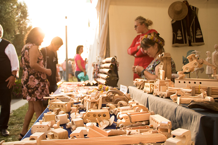 Donaufest 2019: Kunsthandwerkstand mit Holzspielzeug Besucherinnen und Besucher betrachten handgefertigte Holzspielzeuge und Holzarbeiten an einem Marktstand beim Donaufest 2019.