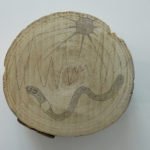 Runder Holzquerschnitt mit eingeritzten Linien, einer sternförmigen Markierung und einer geschwungenen dunklen Form
