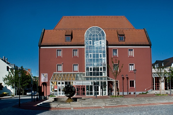 Roter Museumsbau mit gläsernem Eingangsbereich, Freitreppe und Skulptur vor dem Handwerksmuseum in Deggendorf