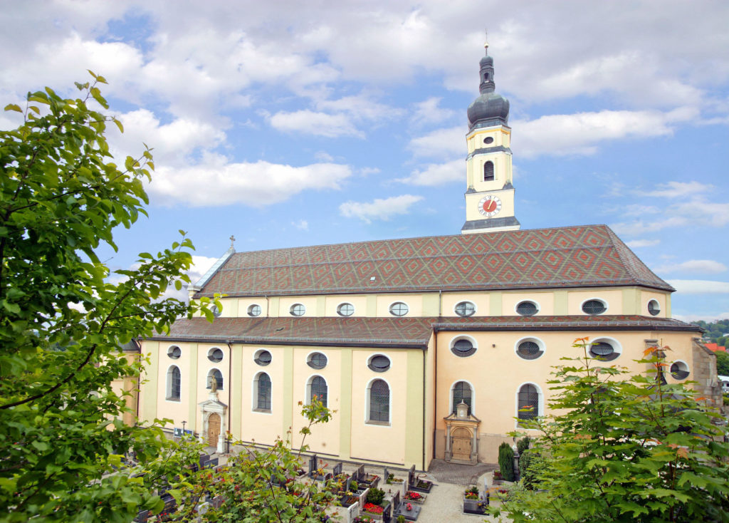 Pfarrkirche Mariä Himmelfahrt mit Gräbern Barocke Pfarrkirche Mariä Himmelfahrt mit Zwiebelturm und angrenzendem Friedhof unter blauem Himmel