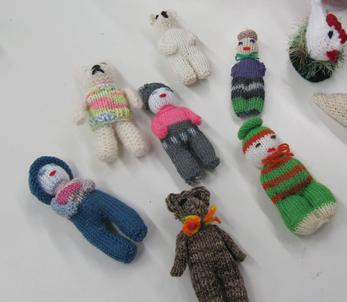 Mehrere handgestrickte Figuren in verschiedenen Farben liegen auf einer weißen Fläche.