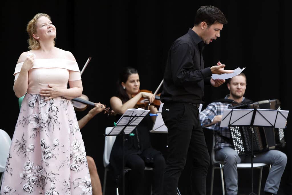 Sängerin und Musiker bei einem Konzertauftritt mit Streichinstrumenten, Akkordeon und Notenständern auf einer Bühne