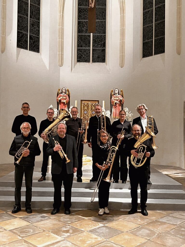 Gruppenfoto des Posaunenchors Deggendorf mit Blechblasinstrumenten vor dem Altar einer Kirche