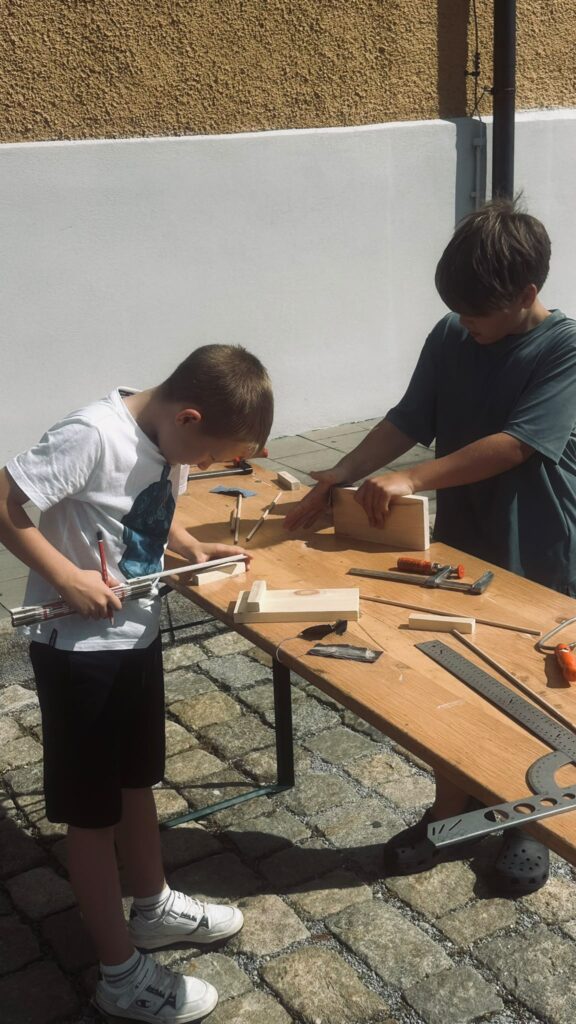 Zwei Kinder bauen an einem Tisch aus Holz eine Handyhalterung.