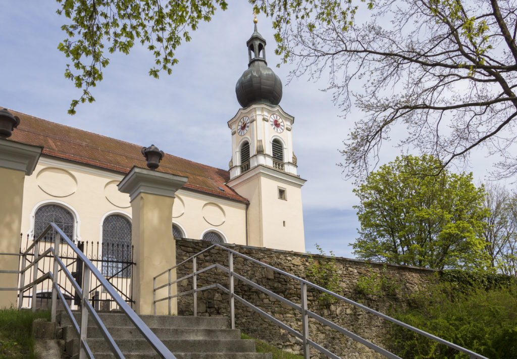 Außenansicht der Kirche St. Stephanus mit hellem Fassadenturm, Zwiebelturm und Treppe mit Metallgeländern