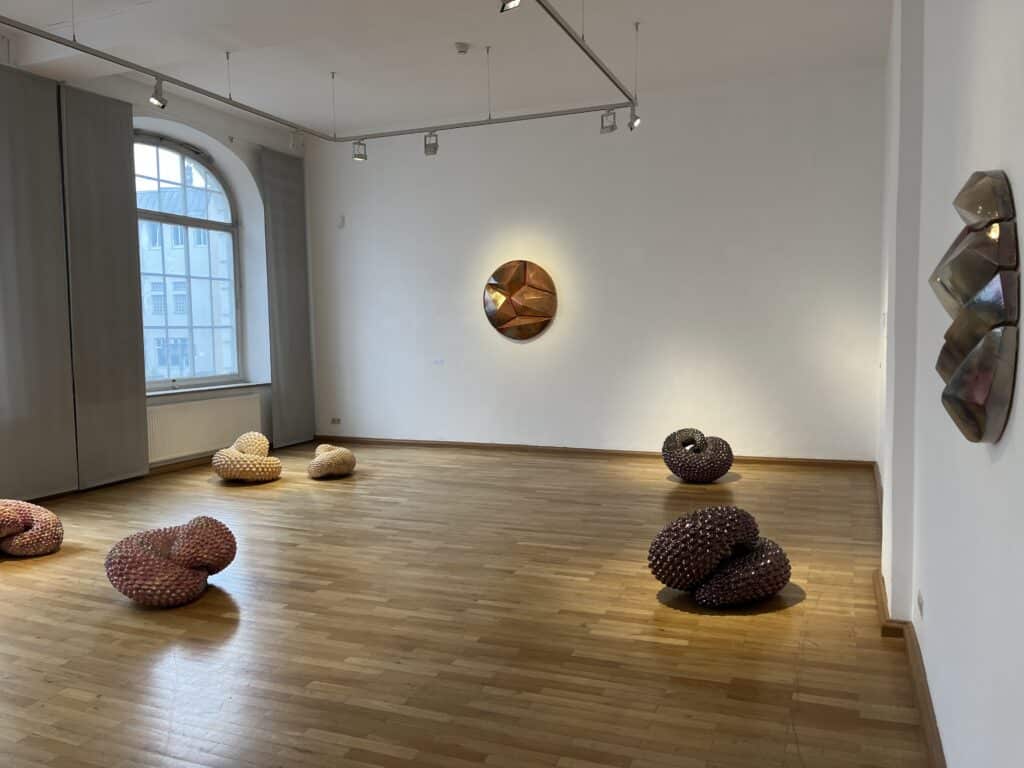 Heller Ausstellungsraum mit mehreren organisch geformten Skulpturen auf dem Parkettboden, an der Wand und neben einem großen Fenster.