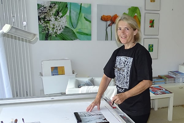 Maria Maier beim Kinderworkshop in Deggendorf Maria Maier steht in einem hellen Atelierraum an einem Arbeitstisch mit Druckgrafiken und Kunstmaterialien.