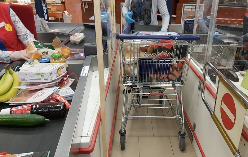 Einkaufswagen mit Lebensmitteln neben einem Kassenband im Supermarkt