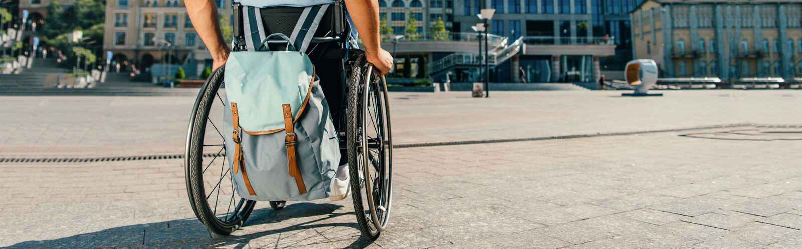 Mensch im Rollstuhl auf einem Platz Person im Rollstuhl mit Rucksack auf einem gepflasterten Platz in Deggendorf