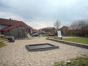 Sandspielplatz mit Klettergerüst, Rutsche und Sitzbereich zwischen Wohnhäusern