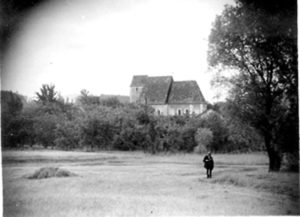 Historische Ansicht von Schaching mit Kirche Historische Schwarz-Weiß-Aufnahme einer Kirche hinter einer Wiese und Bäumen in Schaching; eine Person steht im Vordergrund.