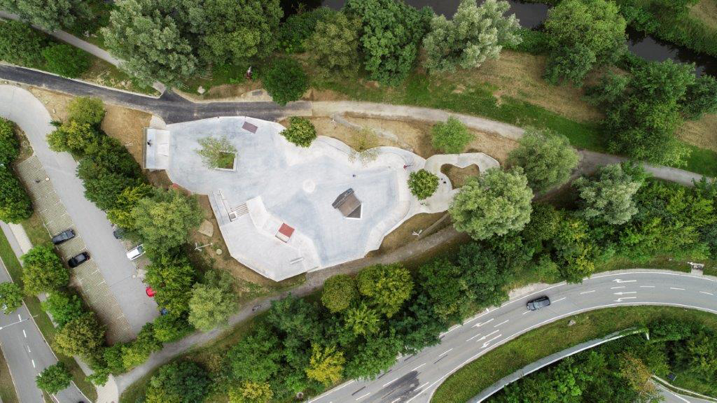 Skateranlage in Deggendorf Luftaufnahme einer begrünten Skateranlage mit geschwungenen Betonflächen, Bäumen, Fußwegen und einer nahe verlaufenden Straße.