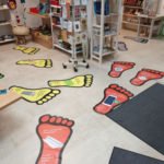 Innenraum eines Weltladens mit Regalen voller Waren und Informationsmaterialien; bunte Fußabdruck-Aufsteller liegen auf dem Boden.
