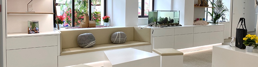Heller Innenraum mit gepolsterter Fensterbank, weißem Mobiliar, Aquarium, Zimmerpflanzen und gelben Blumen