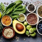 Auswahl an Obst, Gemüse, Nüssen, Samen und Hülsenfrüchten auf dunklem Untergrund