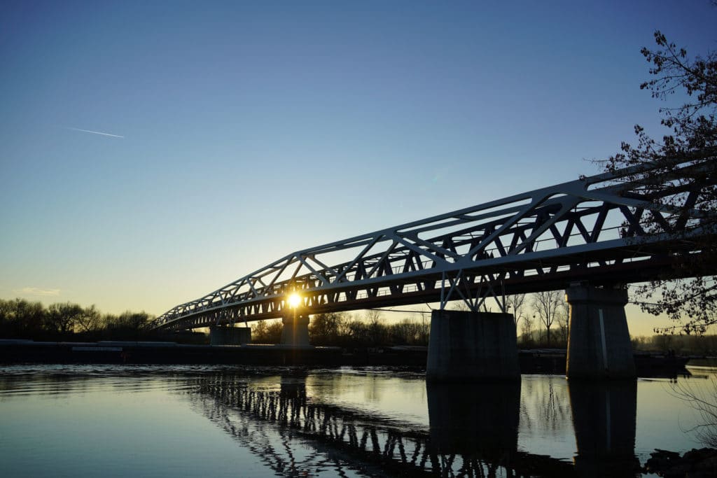 Stählerne Fachwerkbrücke über einem ruhigen Fluss bei tief stehender Sonne