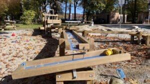 Wasserspielplatz mit Holzrinnen, Wasserlauf, Sand und bunten Spielelementen unter Bäumen