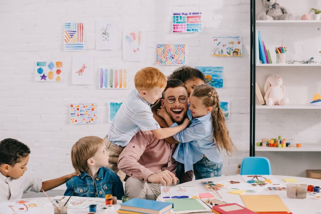 Erwachsene Person und drei Kinder basteln und malen gemeinsam an einem Tisch in einem hellen Kreativraum.