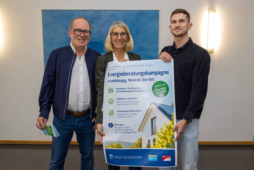 Drei Personen präsentieren ein Plakat zur Energieberatungskampagne für unabhängige und neutrale Energieberatung vor einem blauen Hintergrund.