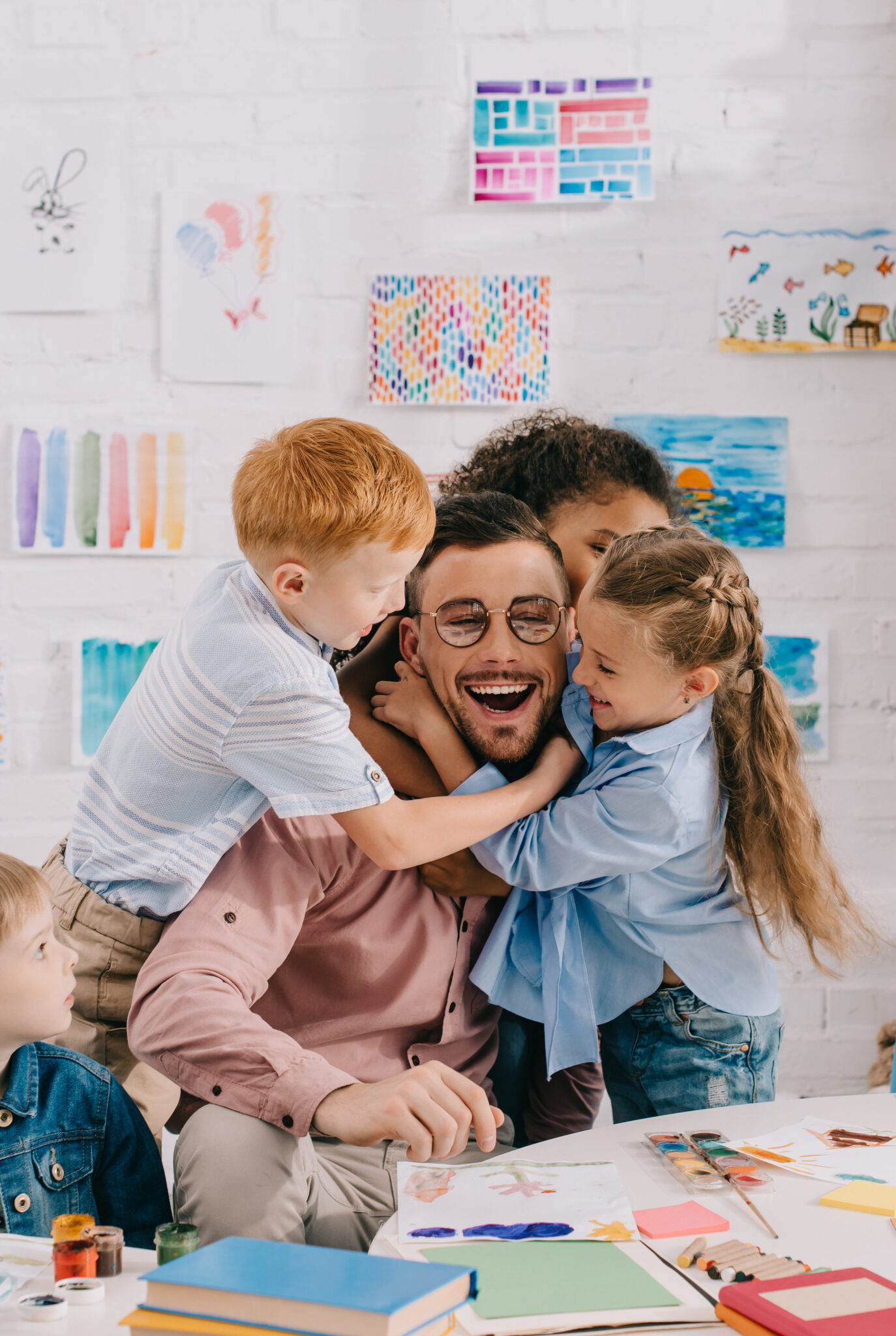 Erwachsene Person und drei Kinder basteln und malen gemeinsam an einem Tisch in einem hellen Kreativraum.