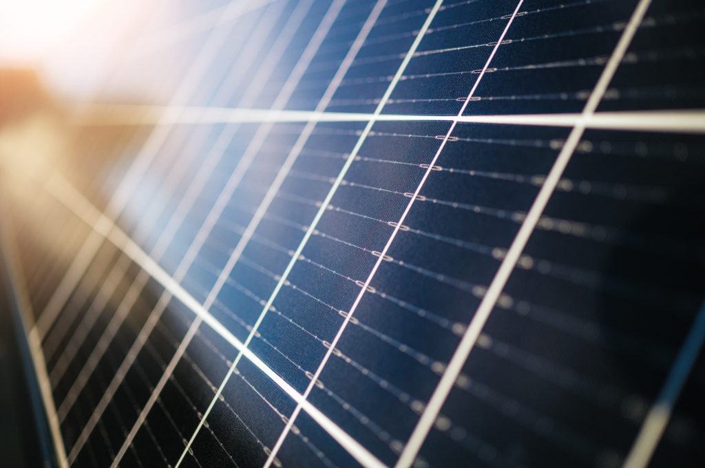 Nahaufnahme einer dunkelblauen Solarzelle mit reflektierenden Metallleitern und einfallendem Sonnenlicht.