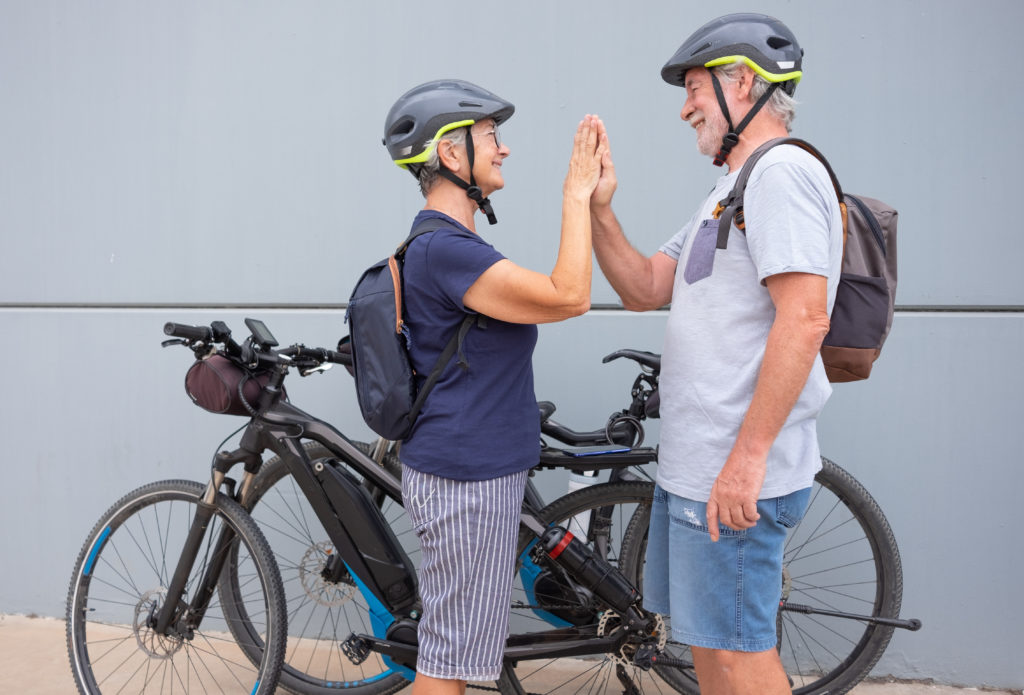 Zwei Erwachsene mit Fahrradhelmen geben sich neben zwei Fahrrädern die Hand zum High Five.