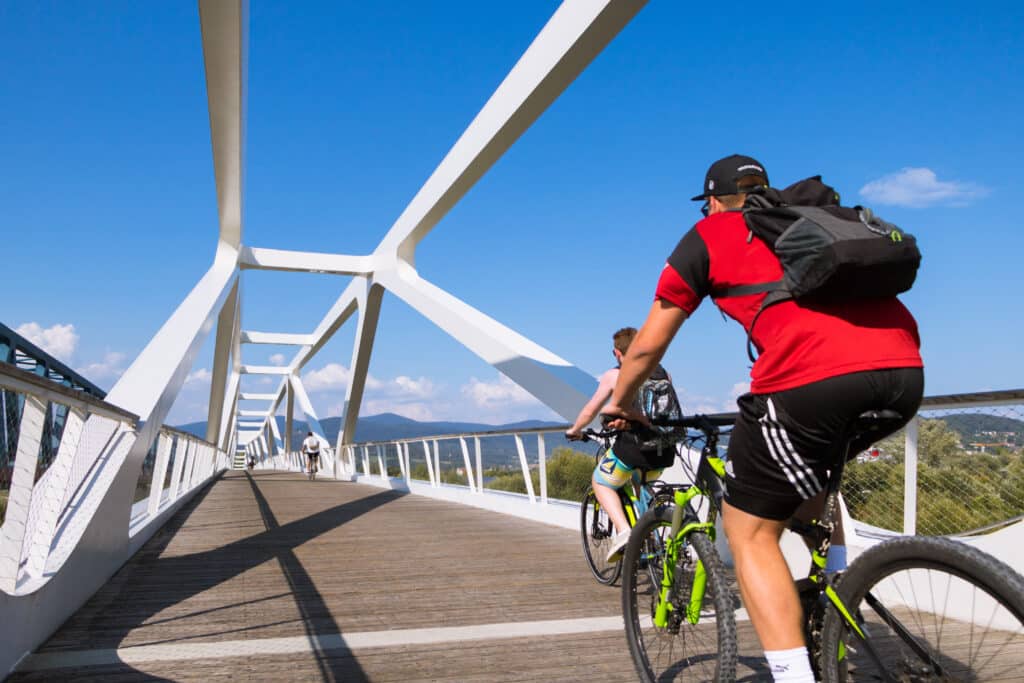 Mehrere Radfahrende überqueren bei blauem Himmel eine moderne Fuß- und Radwegbrücke.