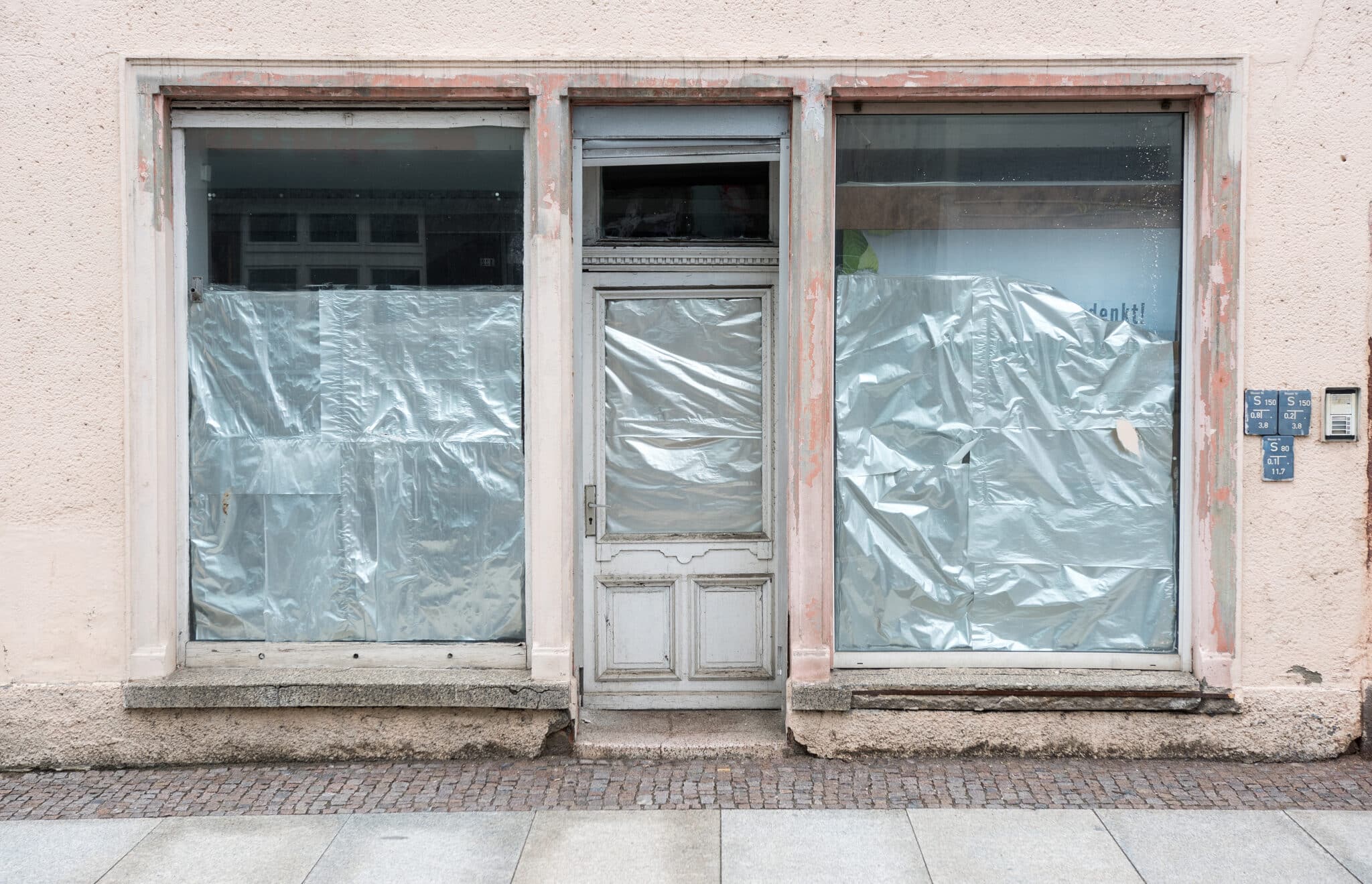 Leerstehende Ladenfront mit abgeklebten Fenstern Eine verschlossene Ladenfront mit zwei großen, mit transparenter Folie abgeklebten Schaufenstern und einer Eingangstür.